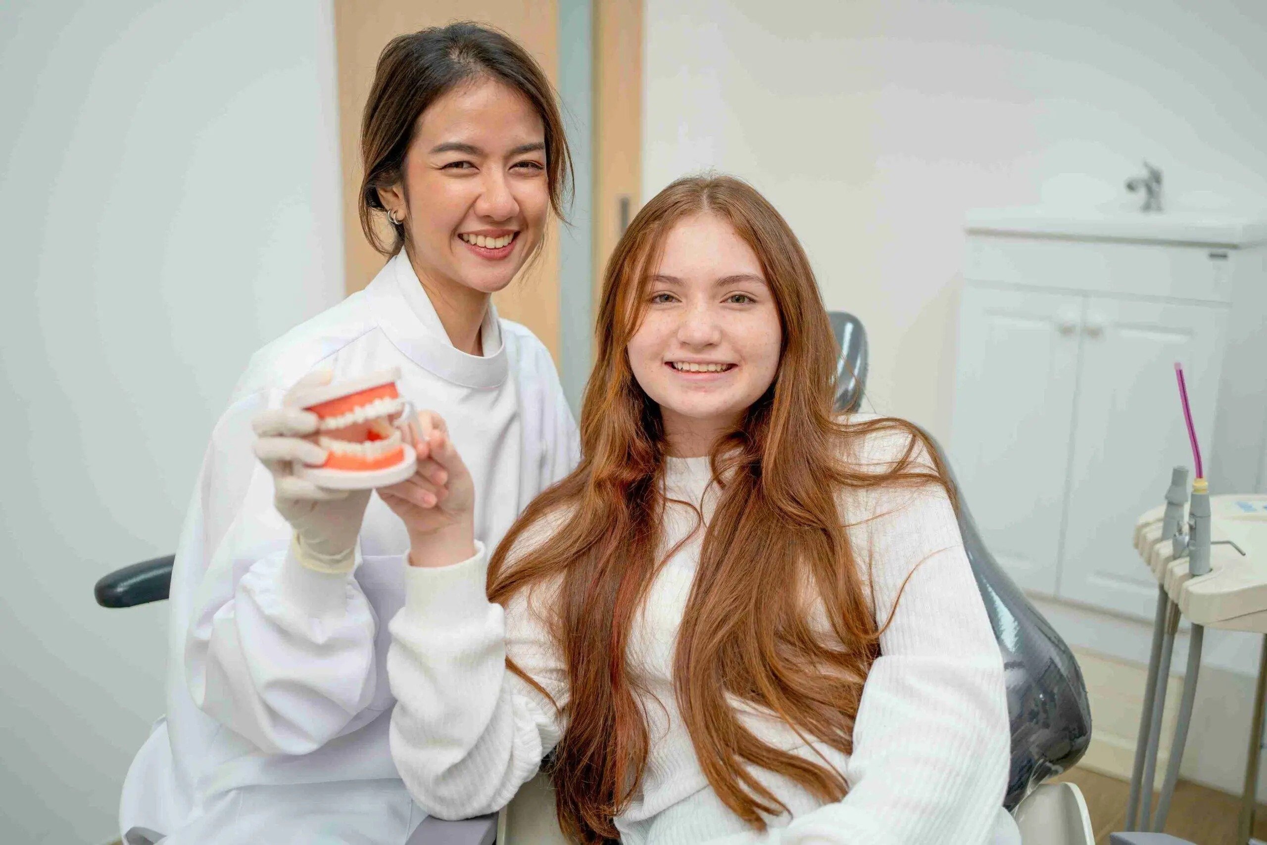 Smiling dentist and young patient holding a dental model in a dental clinic.