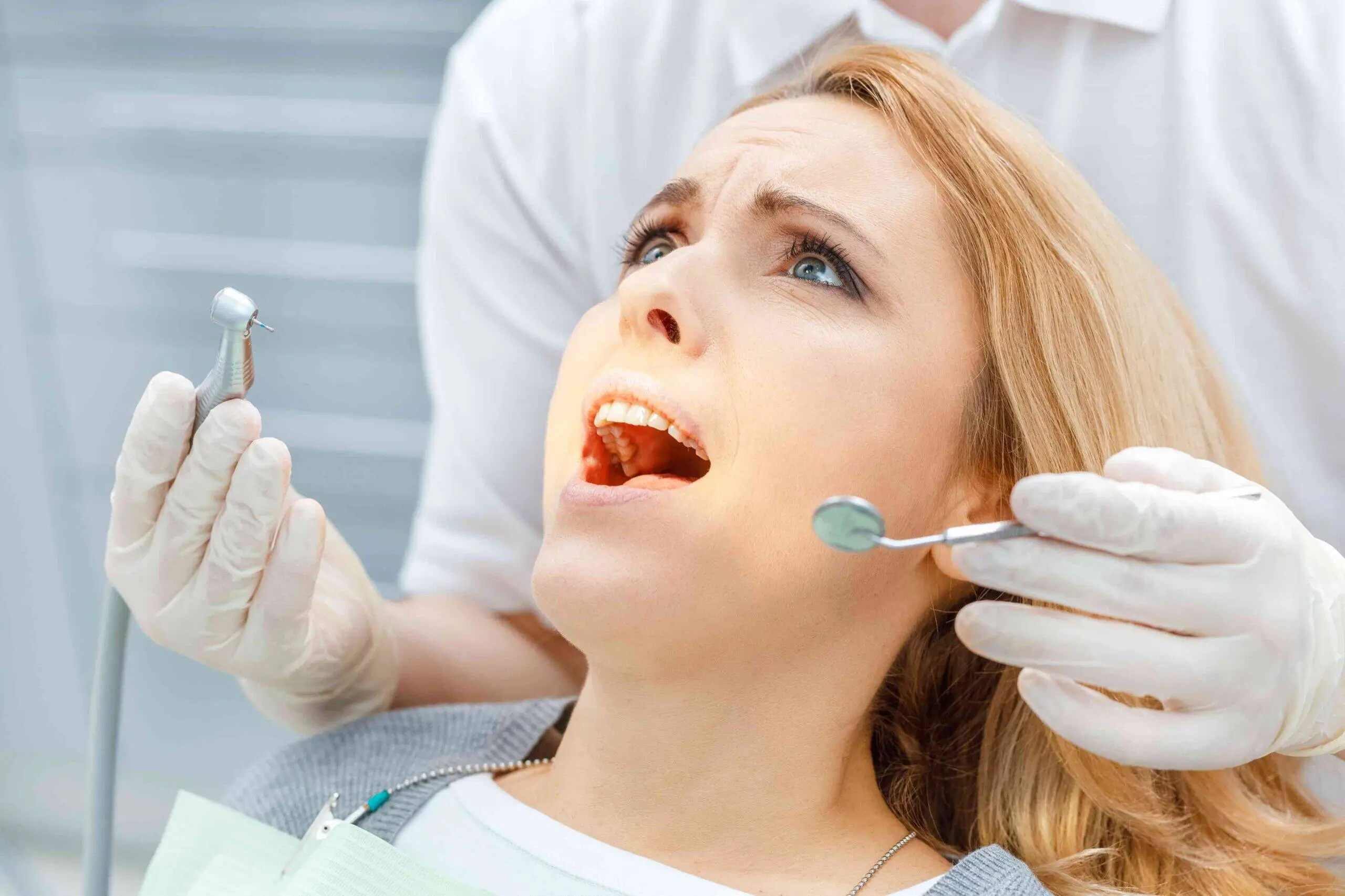Patient receiving a dental examination with mirror and dental drill.