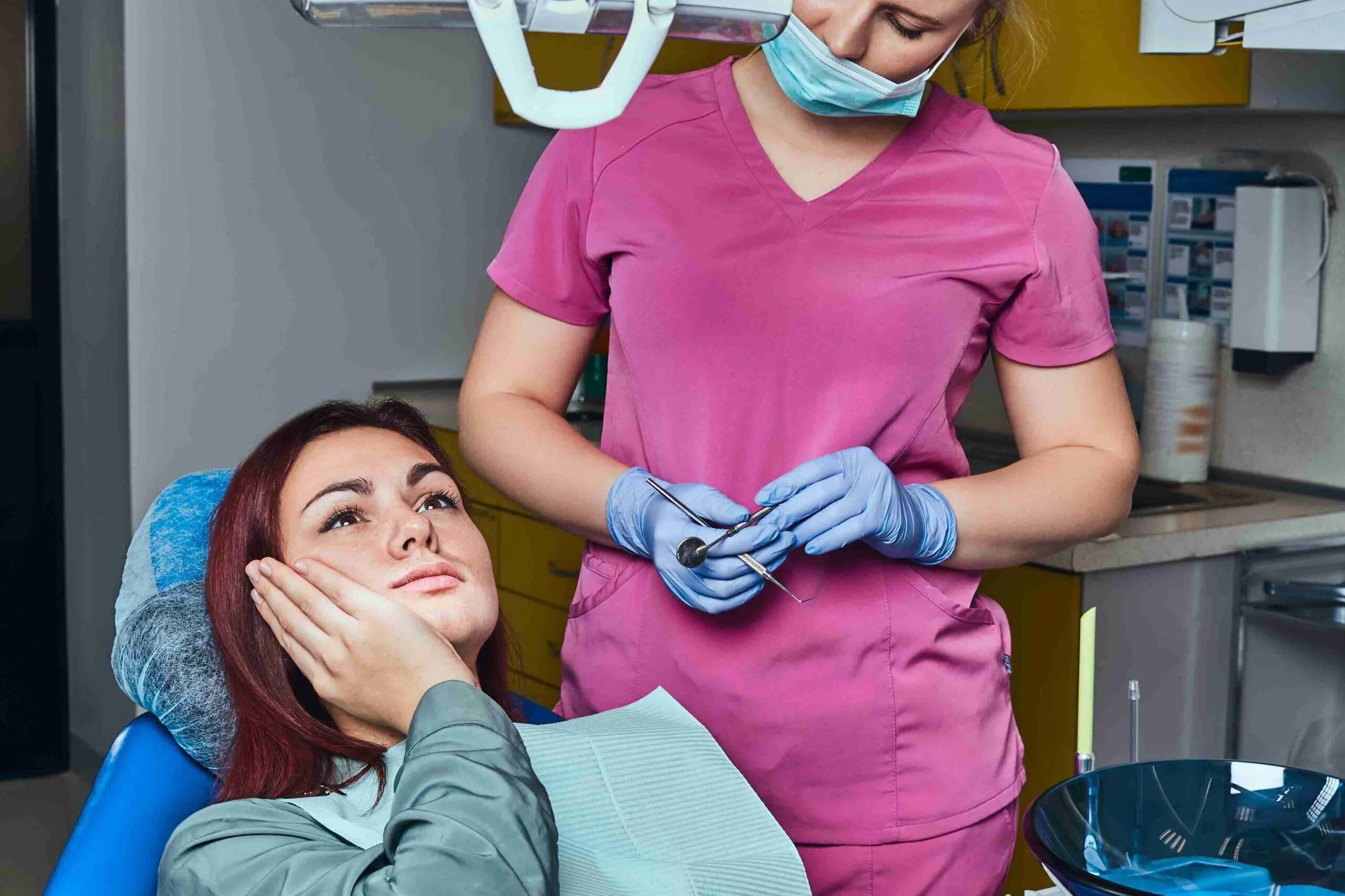 Patient holding her cheek with tooth pain in a dental chair.