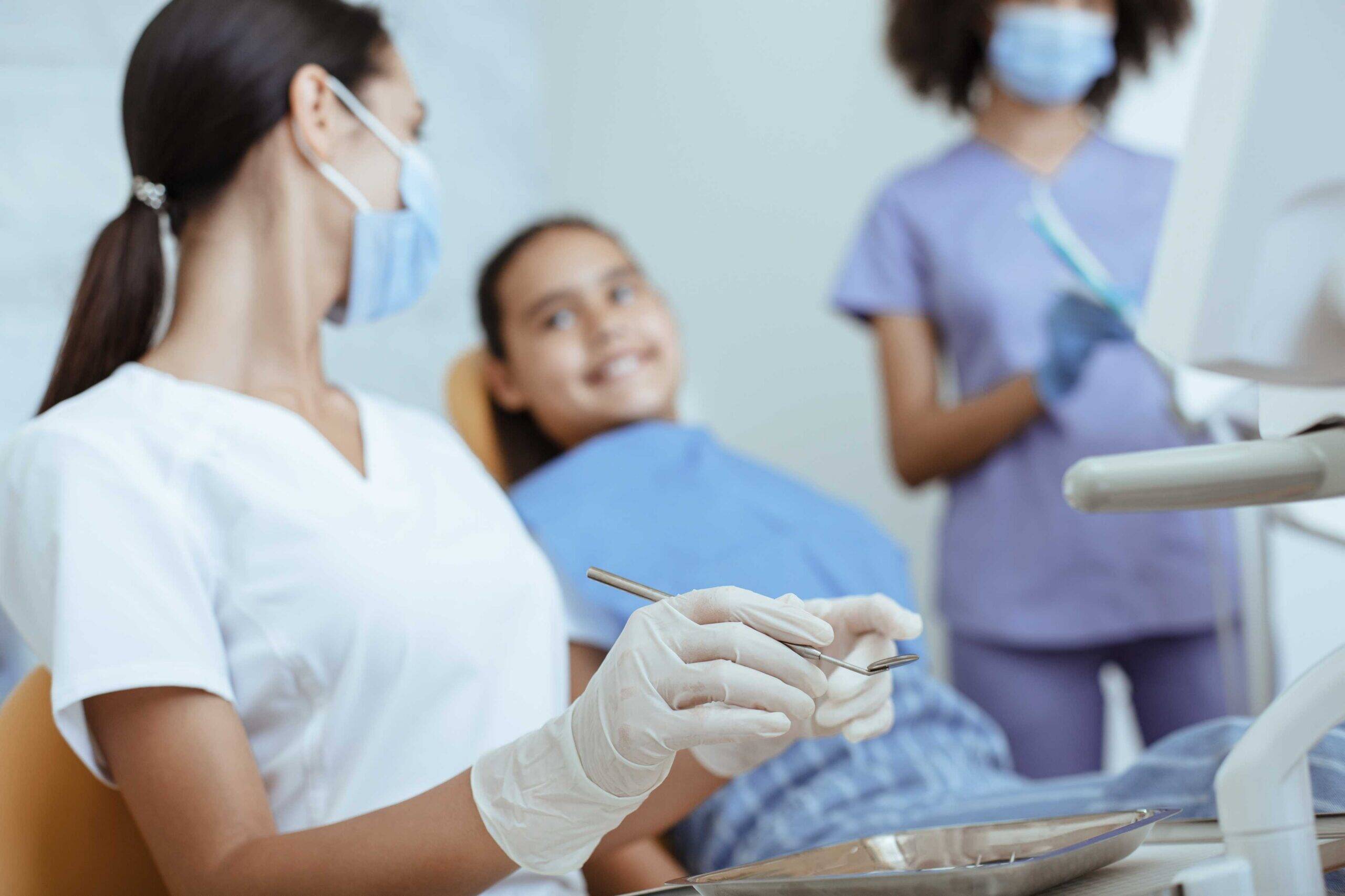 Dentist preparing instruments while a young patient smiles in a dental chair.
